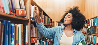 A woman looking taking a book off the shelf while at the library
